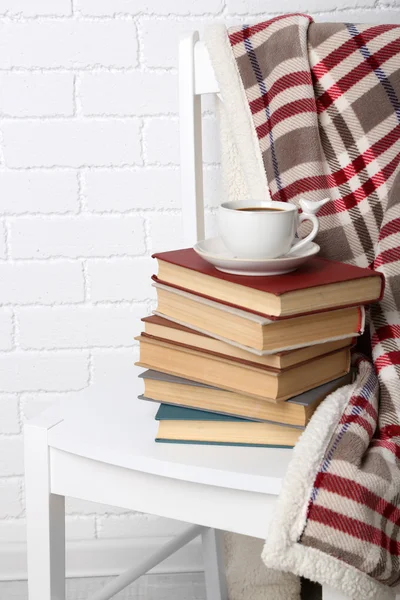 Knih s cup a pléd na židli na cihlovou zeď na pozadí — Stock fotografie