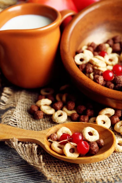 Vari cereali dolci in ciotola, frutta e brocca con latte sul tovagliolo, su sfondo di legno a colori — Foto Stock