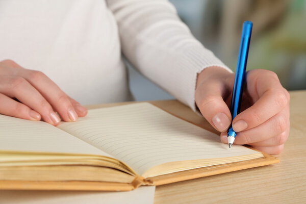 Female hand with pen and notebooks at wooden desktop on light background