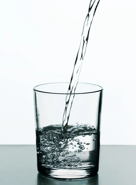 Verter agua de la botella sobre vidrio aislado sobre blanco — Foto de Stock