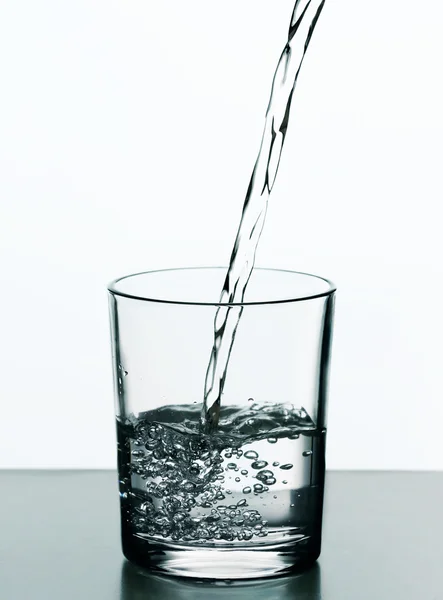 Pouring water from bottle on  glass isolated on white — Stock Photo, Image