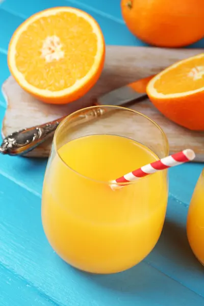 Bicchiere di succo d'arancia con cannucce e fette su tagliere con coltello su fondo di legno a colori — Foto Stock