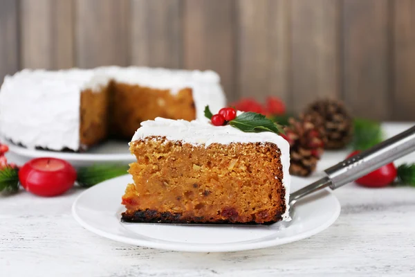 Slice of cake covered cream with Christmas decoration on table, on wooden wall background — Stock Photo, Image