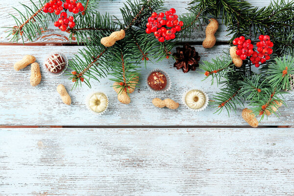Chocolates with hazelnuts and sprigs of Christmas tree on color wooden background