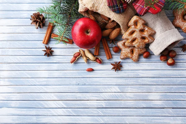 Zweige des Weihnachtsbaums mit Plätzchen, Apfel und Gewürzen auf farbigem Holzhintergrund — Stockfoto