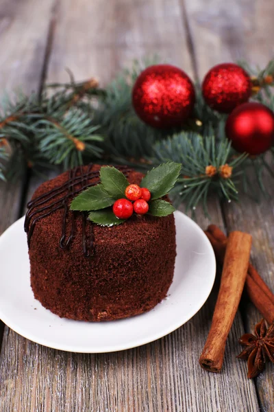 Délicieux gâteau au chocolat sur soucoupe avec houx et baies sur décoration de Noël et fond en bois — Photo
