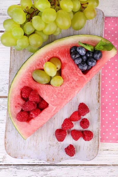 Fresh juicy watermelon slice  with cut out heart shape, filled fresh berries, on cutting board, on wooden background — Stock Photo, Image