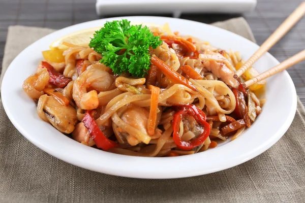 Fideos chinos con verduras y mariscos en plato sobre fondo de estera de bambú —  Fotos de Stock