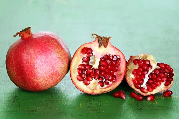 Juicy ripe pomegranates on green wooden table — Stock Photo, Image