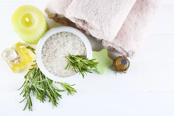 Branches of rosemary and sea salt, towels, candle and bottle with massage oil on color wooden background. Rosemary spa concept — Stock Photo, Image