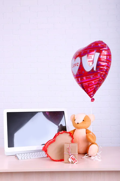 Osito de peluche con cajas presentes y globo de amor en la mesa de madera de la computadora, en el fondo de la pared de ladrillo —  Fotos de Stock