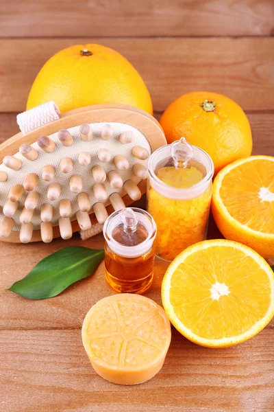 Ripe orange with bottles of bath salt and essential oil, bar of soap and wooden brush on wooden background — Stock Photo, Image