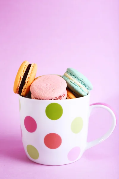 Assortment of gentle colorful macaroons in colorful mug on color background — Stock Photo, Image