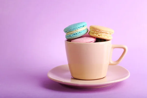 Assortment of gentle colorful macaroons in colorful mug on color background — Stock Photo, Image