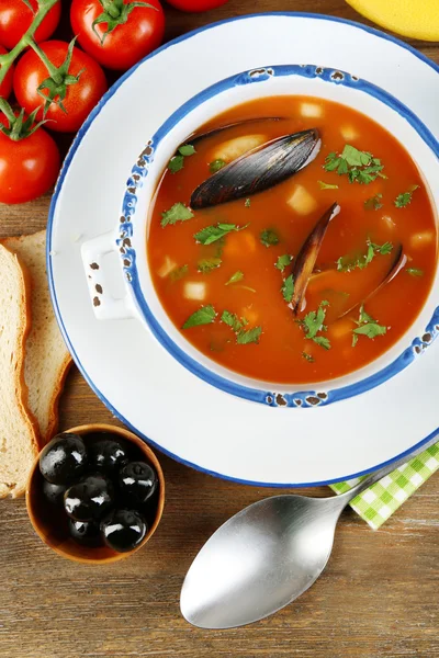 Tasty soup with mussels, tomatoes and black olives in bowl on wooden background — Stock Photo, Image