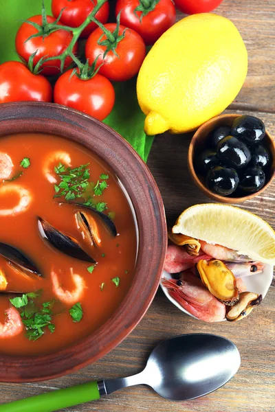 Tasty soup with shrimps, mussels, tomatoes and black olives in bowl on wooden background — Stock Photo, Image