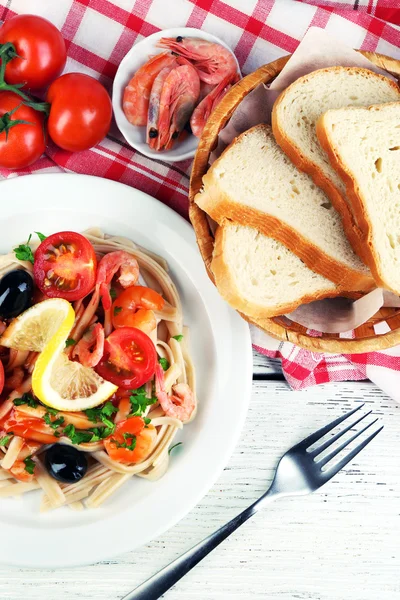 Leckere Pasta mit Garnelen, schwarzen Oliven und Tomatensauce auf Teller auf Holzgrund — Stockfoto