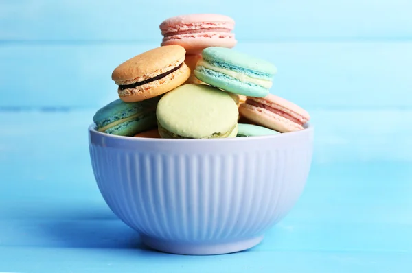 Assortimento di dolci macaron colorati in ciotola colorata su sfondo di legno a colori — Foto Stock