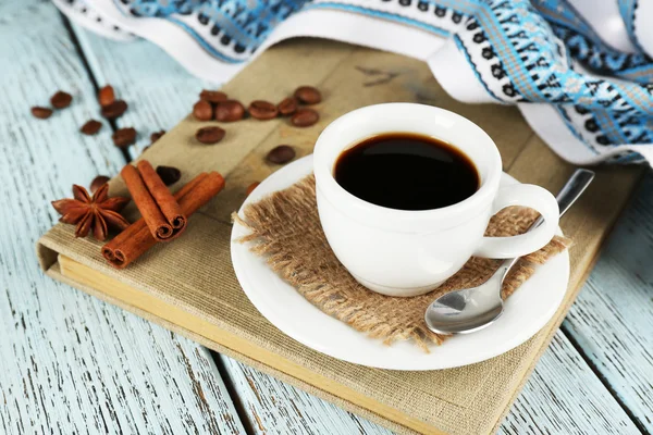 Taza de café en libro con mantel, anís estrellado, granos de café y canela sobre fondo de madera de color — Foto de Stock