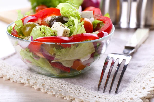 Griechischer Salat in Glasschale mit Gabel und Gemüsehintergrund — Stockfoto