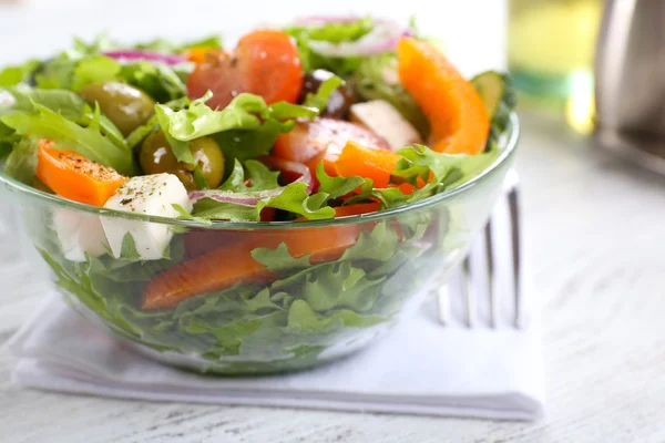 Greek salad in glass dish on napkin and color wooden background — Stock Photo, Image