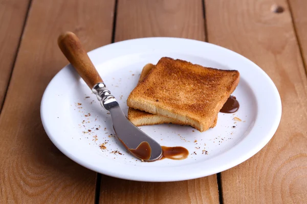 Pan tostado con chocolate en plato con cuchillo sobre fondo de mesa de madera — Foto de Stock