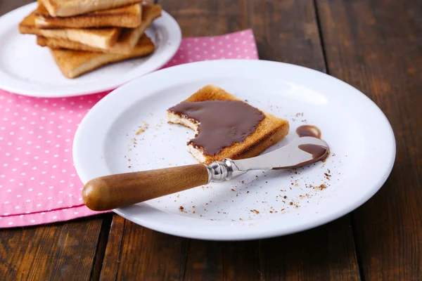 Torrada pão espalhado com chocolate na placa com faca e guardanapo no fundo da mesa de madeira — Fotografia de Stock
