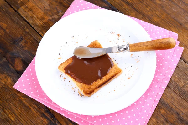 Toast bröd sprids med choklad på tallrik med kniv och servett på träbord bakgrund — Stockfoto