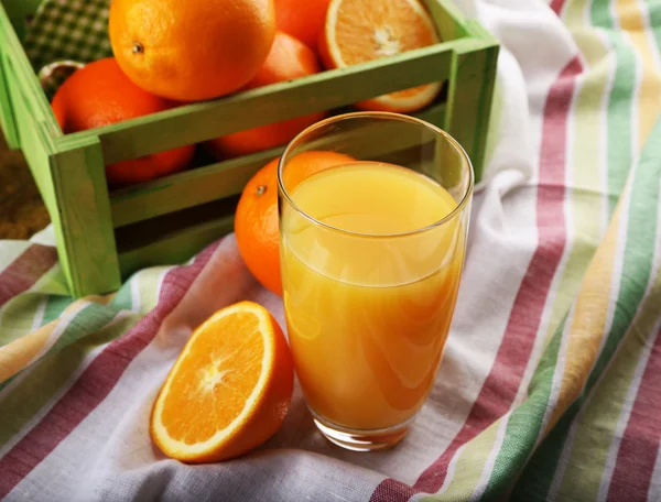 Стекло апельсинового сока с ящиком на полосатой ткани и ломтиками на деревянном фоне стола — стоковое фото