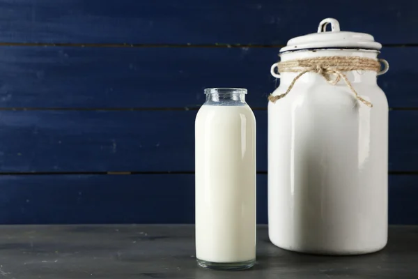 Lattina di latte e bottiglia di vetro su sfondo di legno colore — Foto Stock