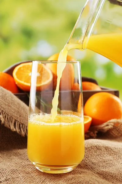 Pouring orange juice from glass carafe, on wooden table and bright background — Stock Photo, Image