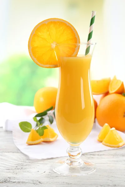 Copo de suco de laranja com palha e fatias na mesa de madeira e fundo brilhante — Fotografia de Stock