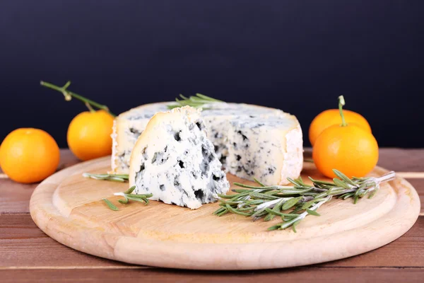 Blue cheese with sprigs of rosemary and oranges on board, wooden table and dark background — Stock Photo, Image