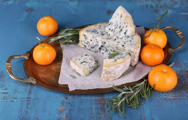 Blue cheese with sprigs of rosemary and oranges on metal tray with sheet of paper and color wooden table background — Stock Photo, Image