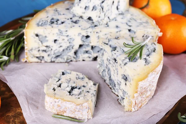 Blauwe kaas met takjes rozemarijn en sinaasappelen op metalen dienblad met vel papier en kleur houten tafel achtergrond — Stockfoto