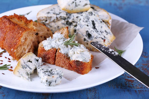 Queijo azul com raminhos de alecrim, pão e nozes na placa e cor de fundo de mesa de madeira — Fotografia de Stock