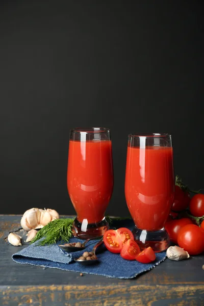 Vasos de sabroso jugo de tomate y tomates frescos sobre la mesa, sobre fondo gris — Foto de Stock