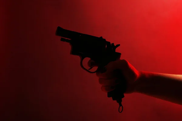 Hand holding gun on red background — Stock Photo, Image