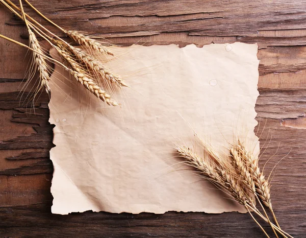 Spikelets of wheat with paper on wooden background — Stock Photo, Image