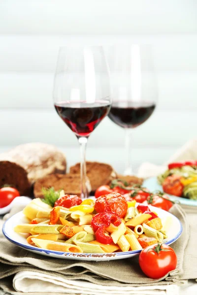 Pasta salad with vegetables and two glasses of red wine on wooden table background — Stock Photo, Image