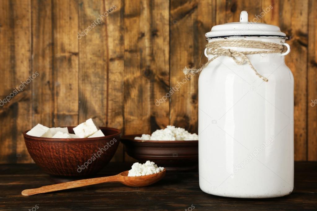 Milk can with bowl of cottage cheese and spoon on rustic wooden background