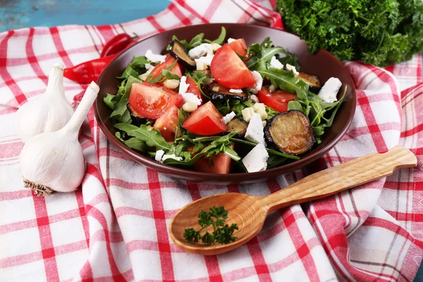 Eggplant salad with tomatoes, arugula and feta cheese, on napkin, on color wooden background — Stock Photo, Image