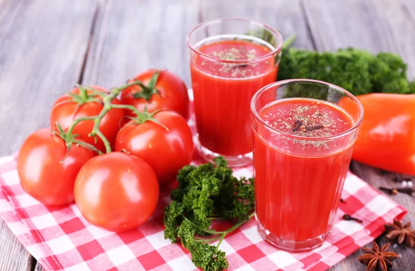 Tomato juice in glasses and fresh vegetables on napkin on wooden background — Stock Photo, Image