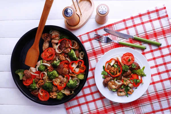 Тушковані дикі гриби з овочами та спеціями на сковороді та тарілкою на столі — стокове фото