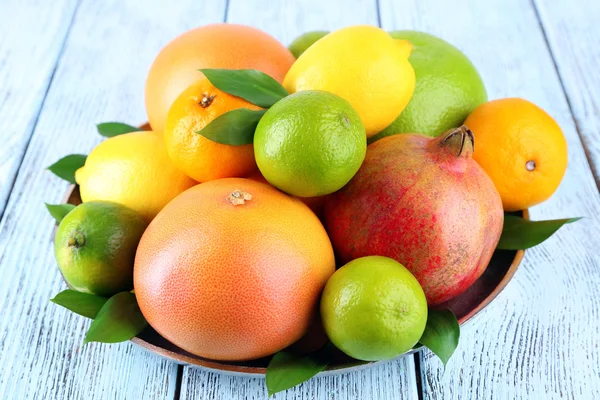 Rijp citrus met groene bladeren op plaat op houten achtergrond — Stockfoto