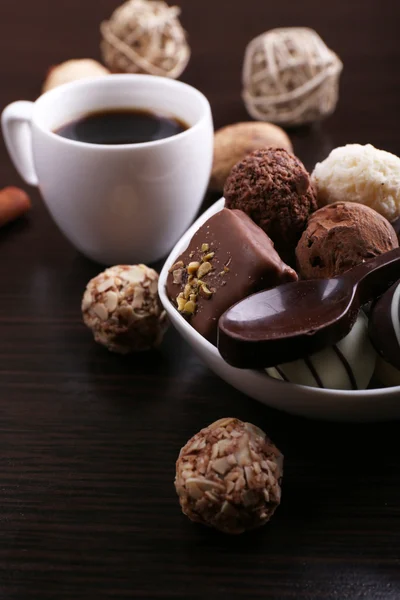 Una taza de café con chocolates y cuchara dulce sobre el fondo liso de madera oscura —  Fotos de Stock
