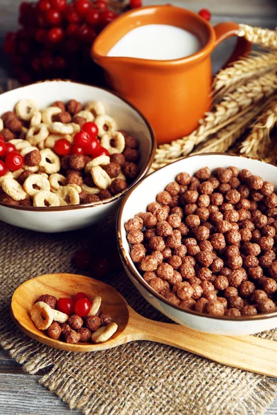 Varios cereales dulces en tazones de cerámica, frutas y jarra con leche en la servilleta, sobre fondo de madera de color —  Fotos de Stock