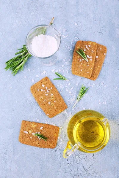 Knäckebröd met zout, kruik van olie en takjes rozemarijn op een houten tafel achtergrond kleur — Stockfoto