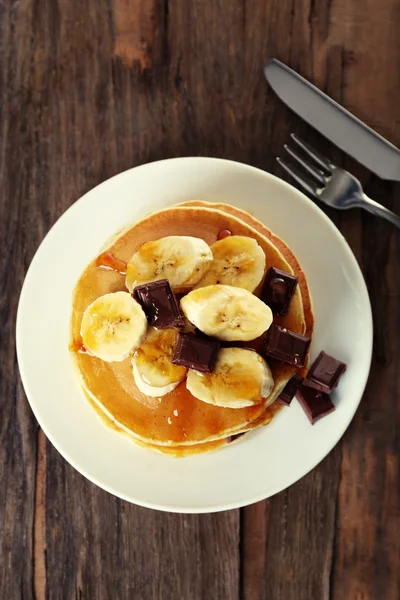 Bunt med läckra pannkakor med choklad, honung och skivor av banan på plattan på träbord bakgrund — Stockfoto