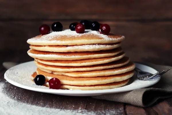 Stapel leckerer Pfannkuchen mit Puderzucker und Beeren auf Teller und Serviette auf Holzgrund — Stockfoto
